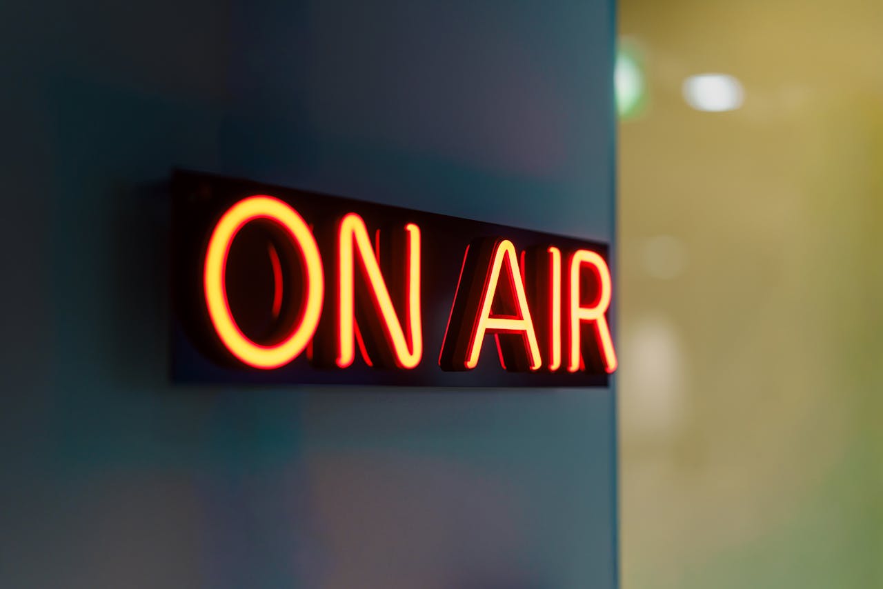 Close-up of a glowing 'On Air' neon sign in a dimly lit studio setting, symbolizing live broadcasting.